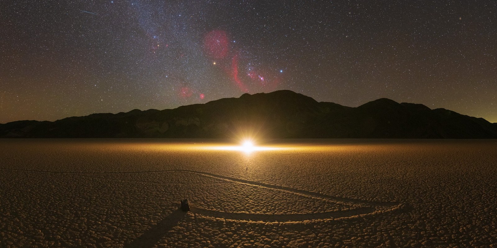 Milky Way and a bright light on the horizon above a moving rock in Death Valley
