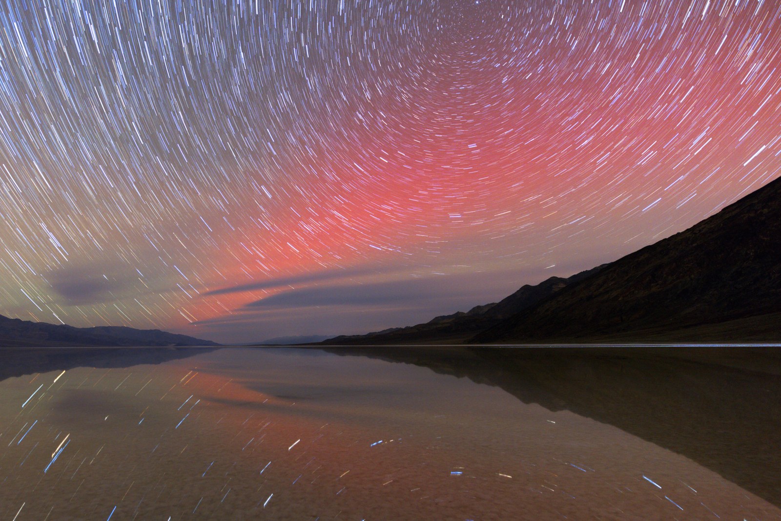 Red auroral arc and star trails over lake