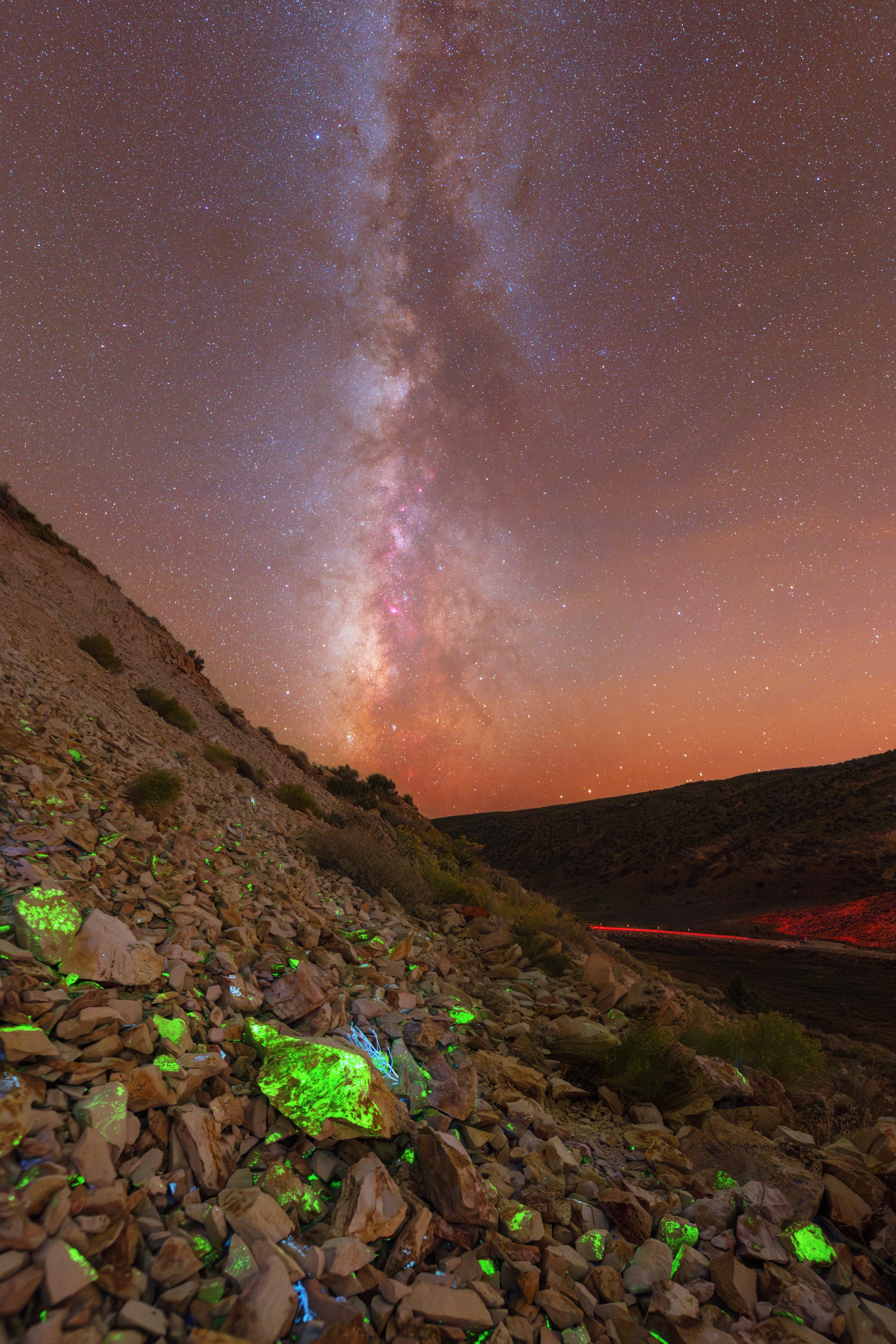 Milky Way above an abandoned uranium mine, with green-lit rocks in the foreground